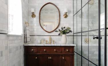 grey marble bathroom with dark cherry wood vanity and oval mirror with glass shower