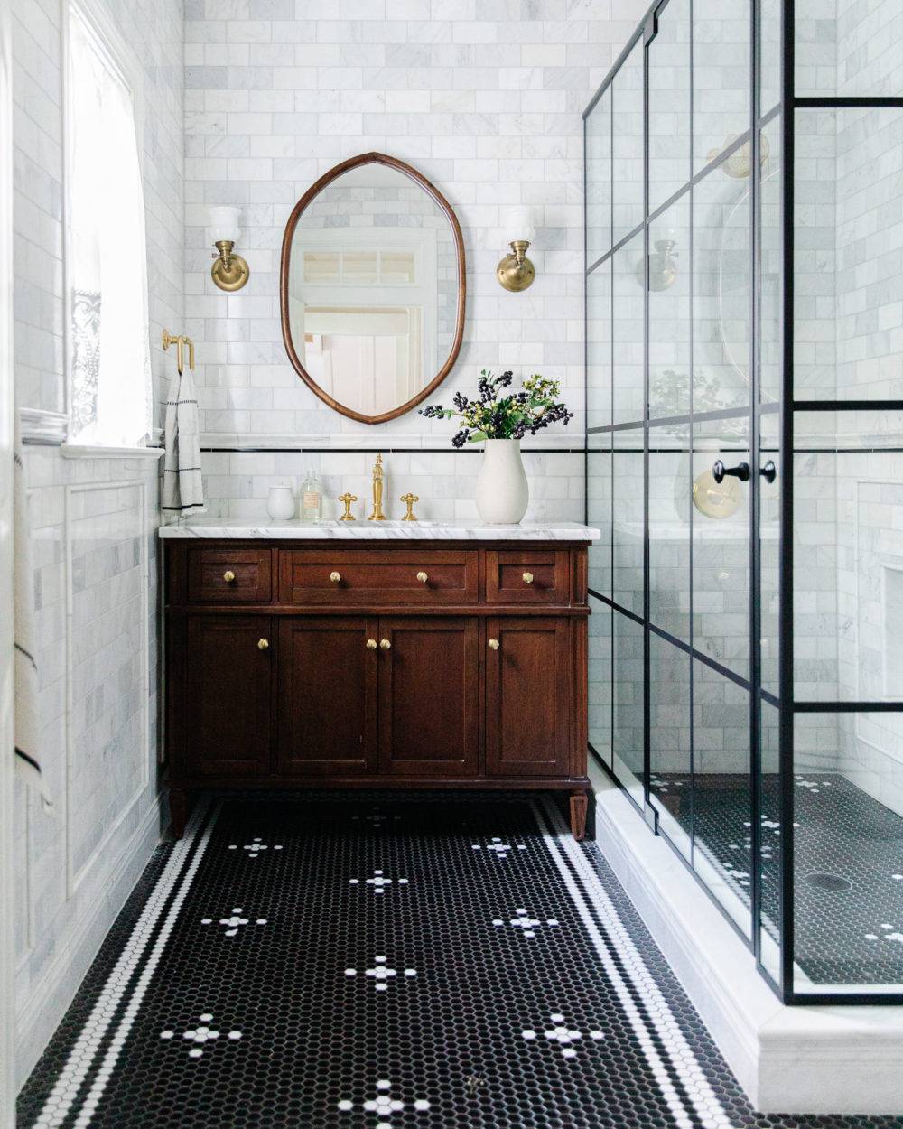 Marble tiled bathroom featuring black and white penny round custom floor pattern and dark wood vanity