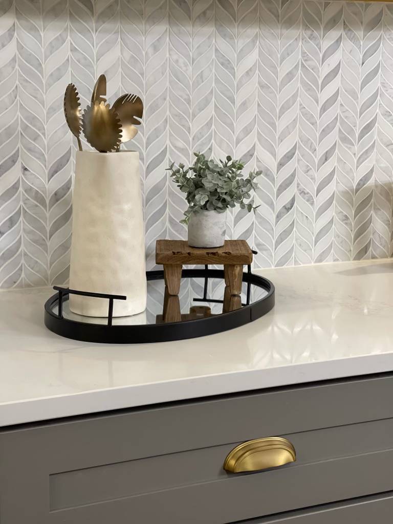White and Grey chevron mosaic tile behind counter with jar of cooking spoons and small plant.