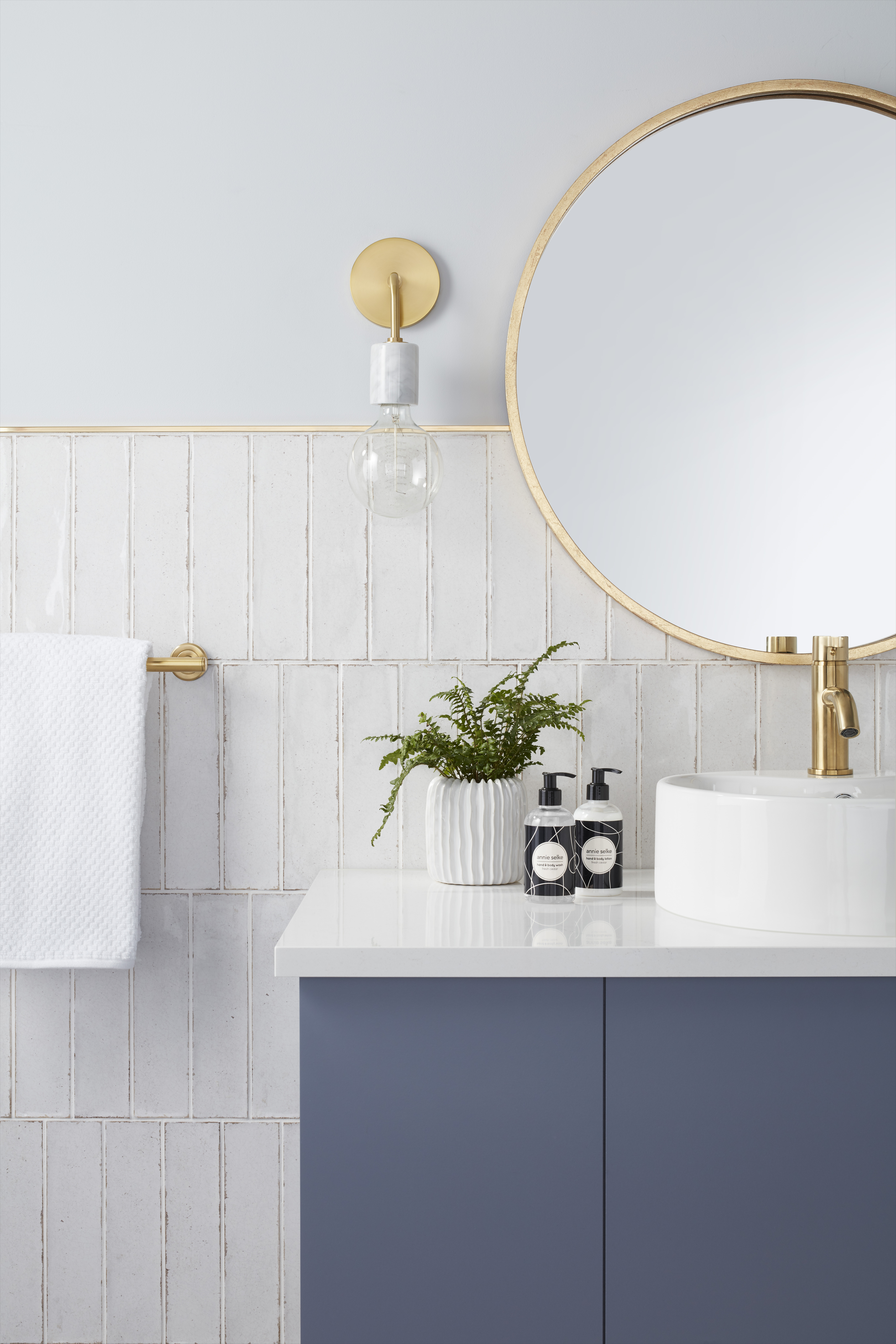 White subway tile wall with gold trim and blue sink vanity with gold faucet. 