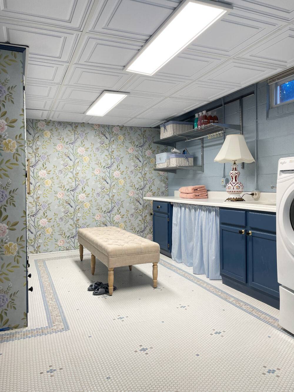 Blue laundry room with beige bench and floral wallpaper. Blue, taupe and white mosaic patterned floor.