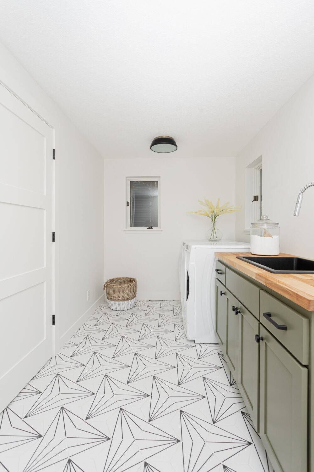 White laundry room with olive green cabinets and black geometric patterned floor tile.