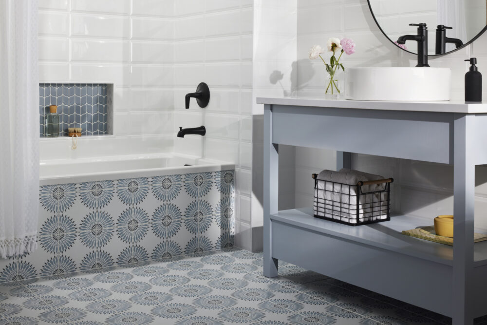 Bathroom with blue and charcoal geometric patterned floor tile, white subway wall tile and blue mosaic shower niche. 