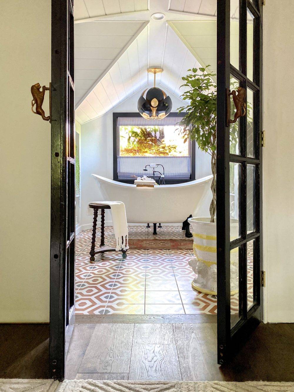 Door opening to large bathroom with orange patterned tile flooring and freestanding bathtub