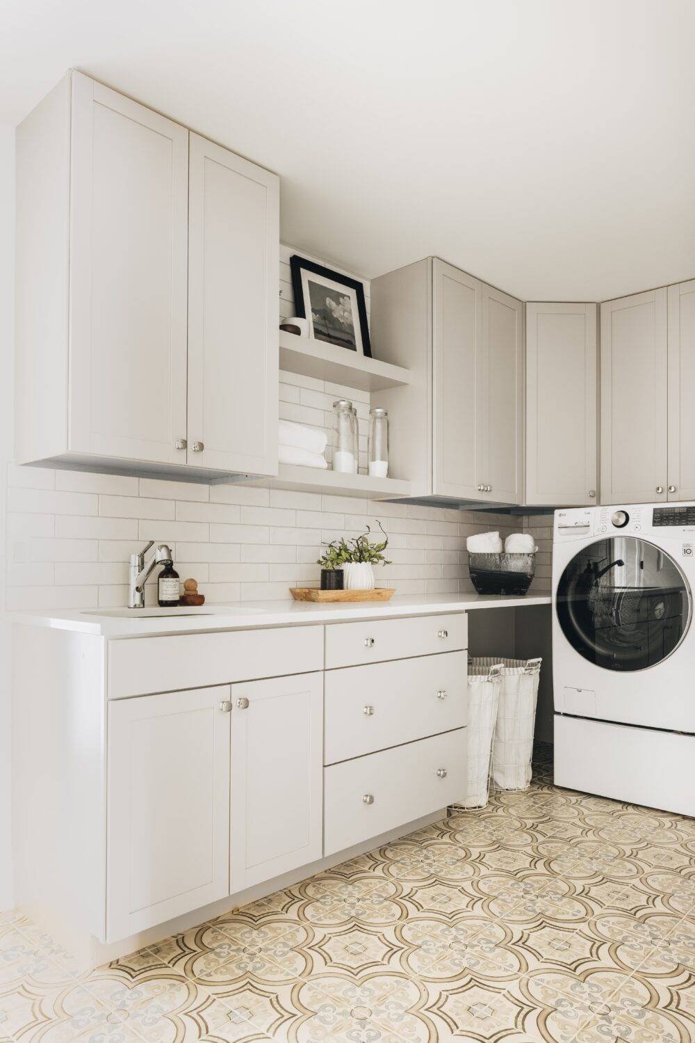 White laundry room with cabinets and patterned floor tile. 
