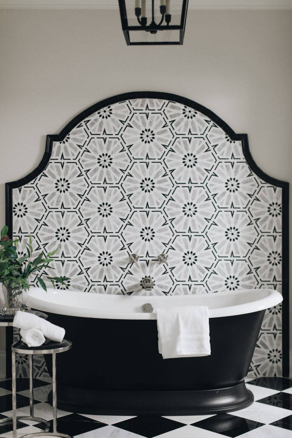 Black, white and grey mosaic tile accent wall with black and white tub and black and white checkerboard marble floor. 