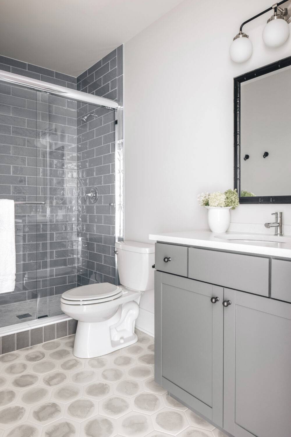 Neutral bathroom featuring Bulevar Grey shower tile and Blot Noon Hexagon floor tile. 