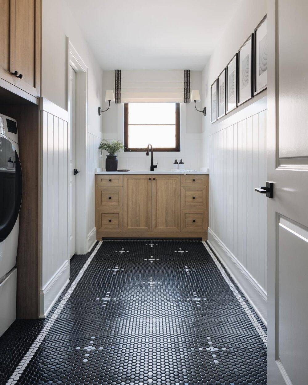 Laundry room with black with a white cross-patterned mosaic floor. Wooden cabinetry. 