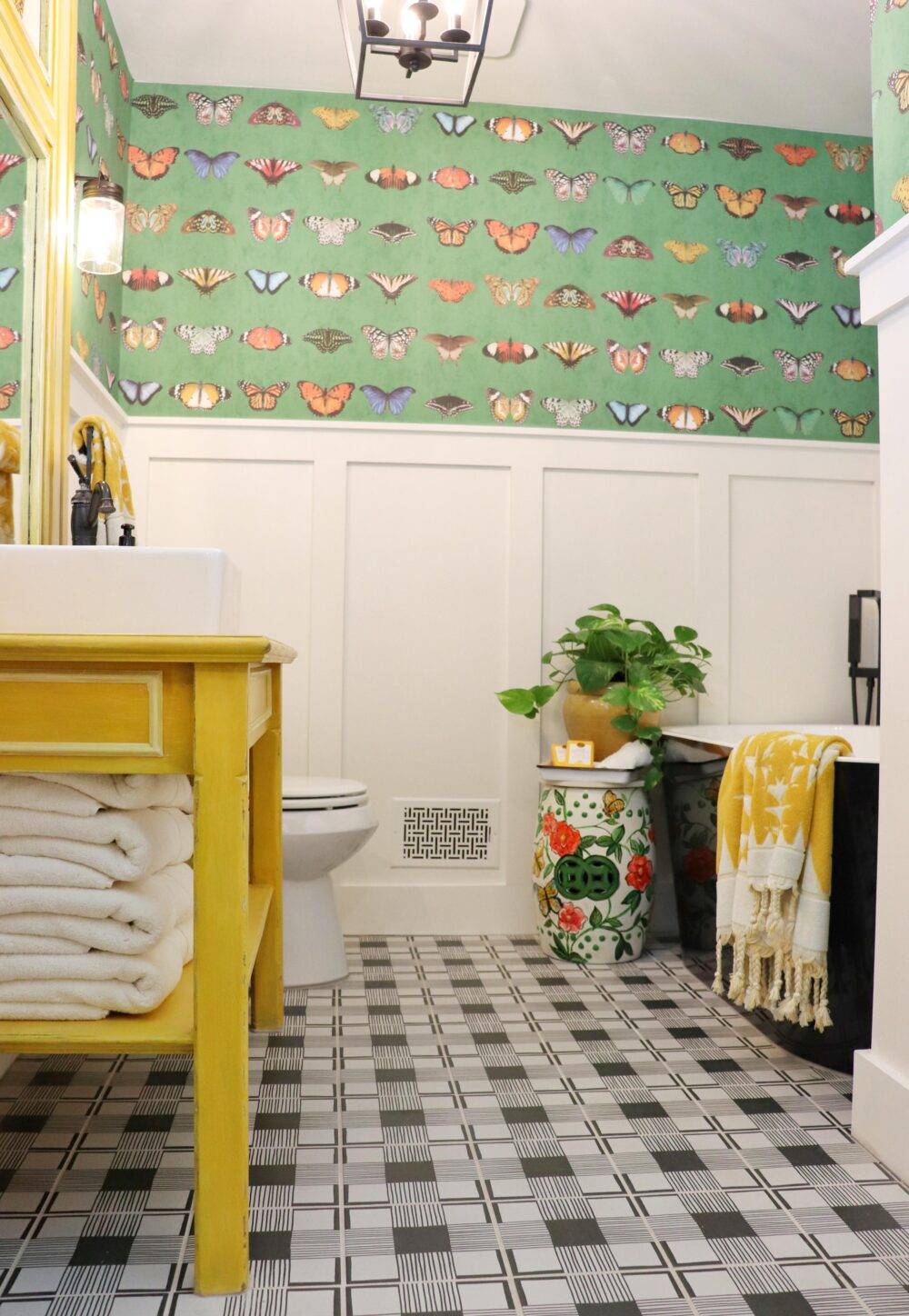 Bright bathroom featuring Cloth Black and White floor tile, with yellow sink and butterfly wallpaper. 